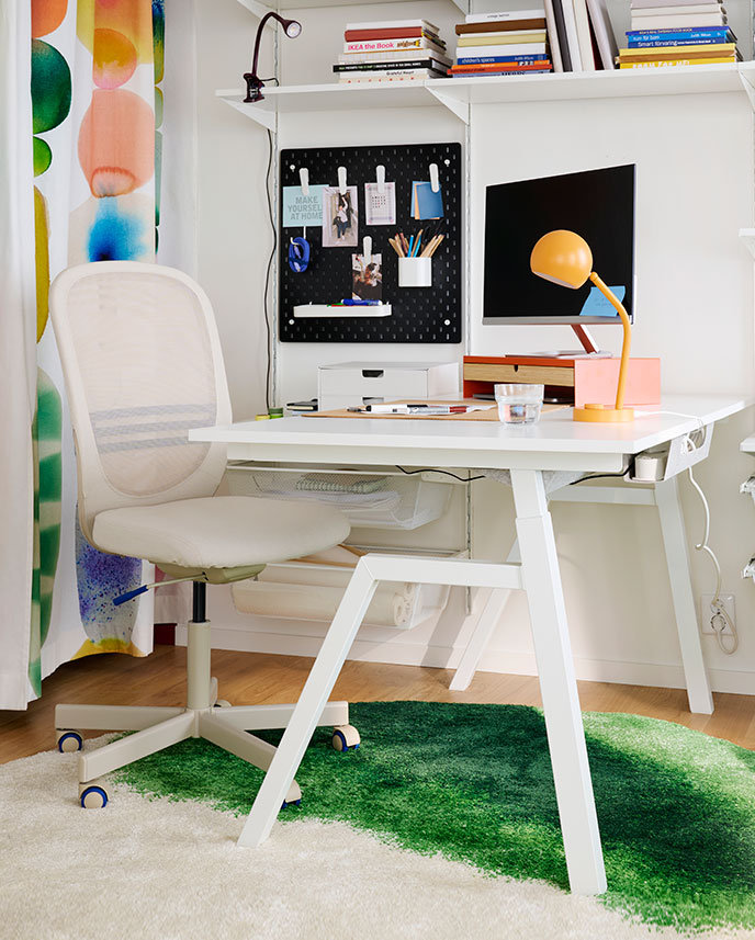 A home office features a white TROTTEN desk sit/stand made from electric material, with a chair beside it.