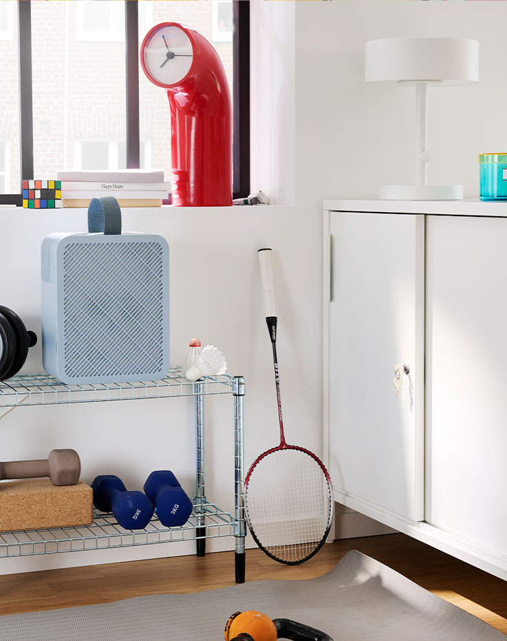 A gym corner features a blue UPPÅTVIND air purifier on a shelf, next to weights and a yoga mat on the floor.
