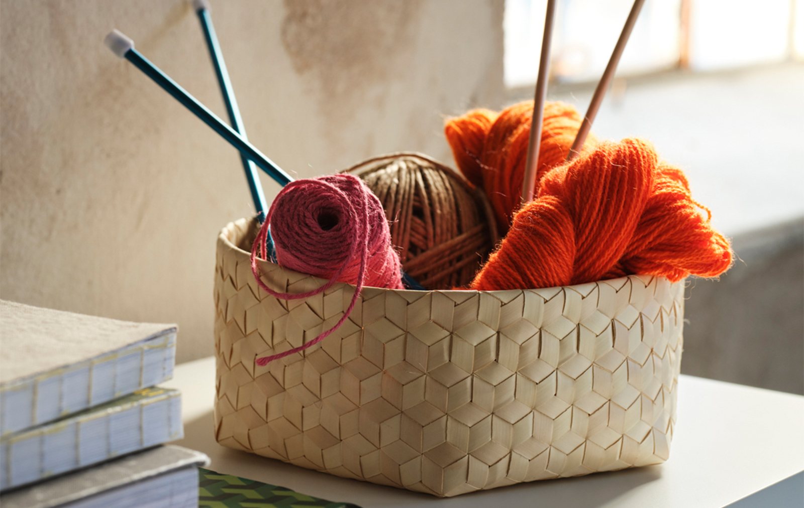 Woven wicker basket filled with colorful yarn skeins and knitting needles.