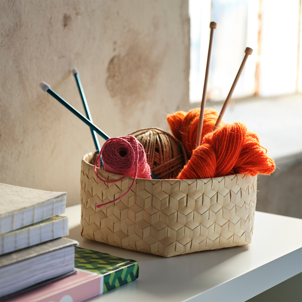 Woven wicker basket filled with colorful yarn skeins and knitting needles.