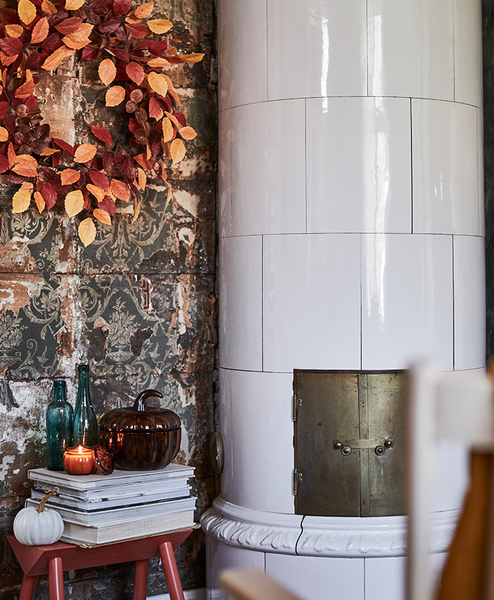 Cozy autumn-inspired corner featuring a white tiled stove, warm decorative accents and rustic textures that create a relaxed and inviting atmosphere.