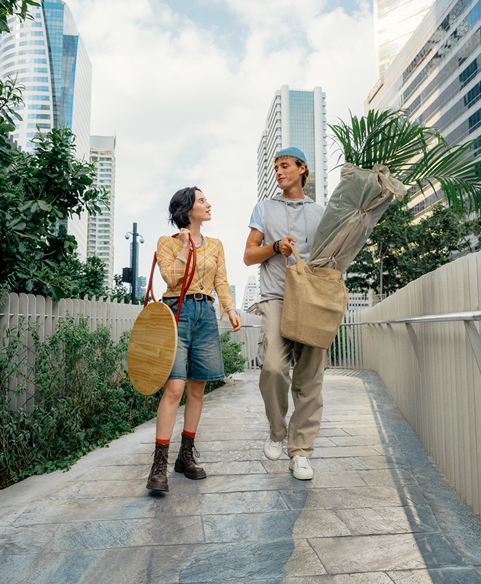 Dos personas caminan juntas por la ciudad llevando una planta y accesorios para el hogar, camino a casa para decorar un nuevo espacio.