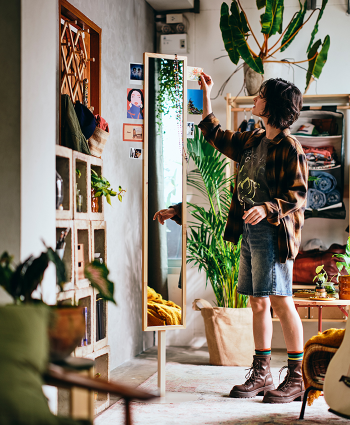 Una persona coloca una planta alta junto a un armario con espejo en un hogar acogedor mientras decora y organiza el espacio.