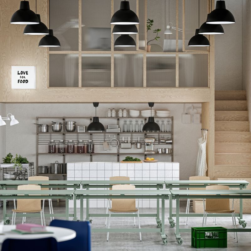 Amplia sala de espera de una oficina moderna y creativa, al fondo se ve una mesa de reuniones con alguien exponiendo, el lugar parece espacioso, luminoso y elegante.