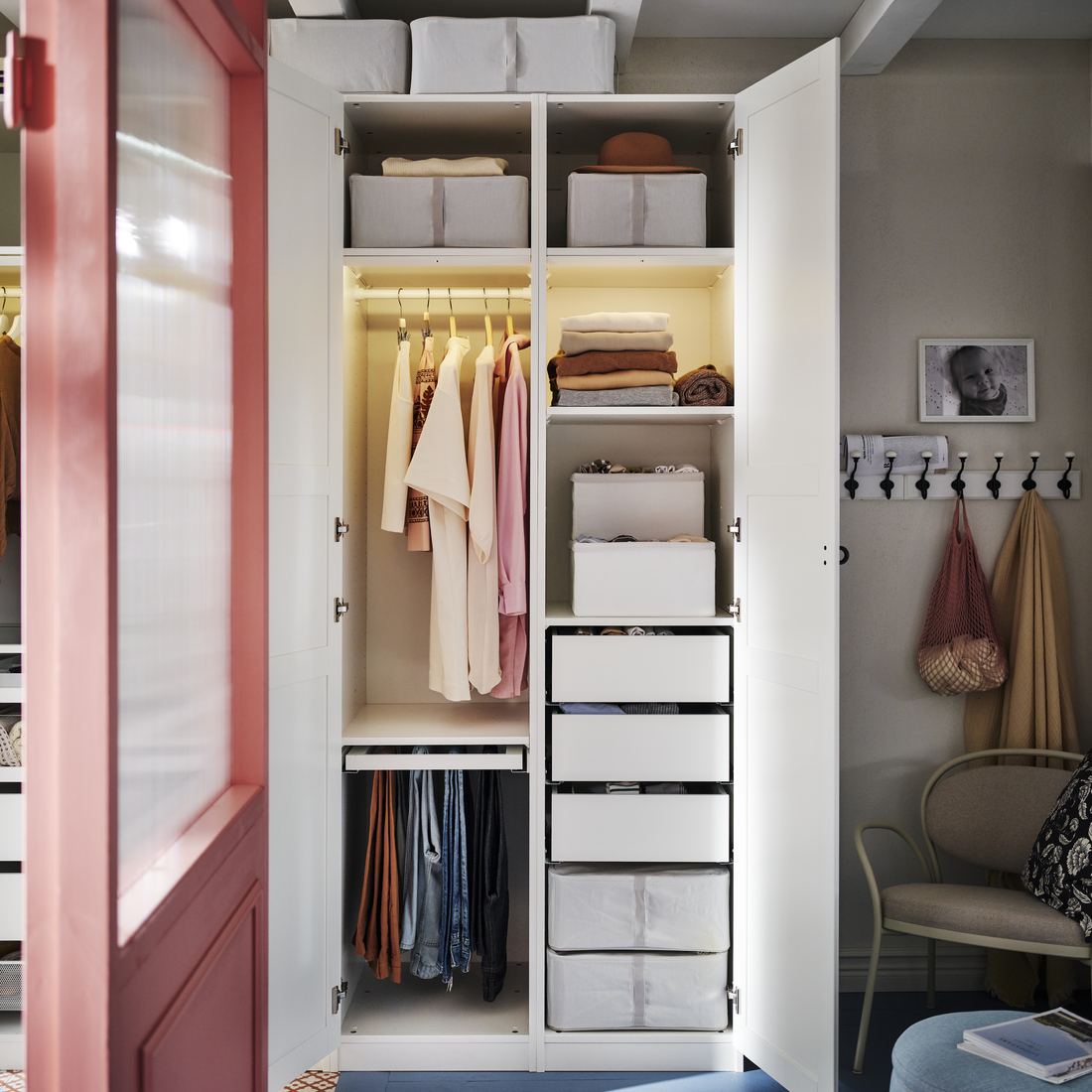 Open illuminated white wardrobe with hanging clothes, drawers, and storage boxes.