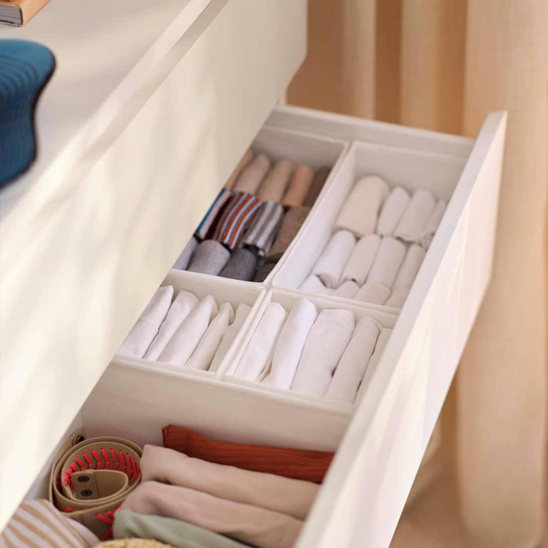 Open white dresser drawer with fabric organizers holding neatly folded clothes.