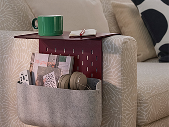 Sofa armrest side table holding a green mug and a felt organizer pocket.