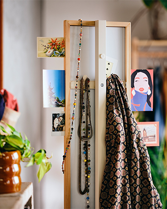 Standing wooden mirror decorated with hanging necklaces, a patterned scarf, and postcards.