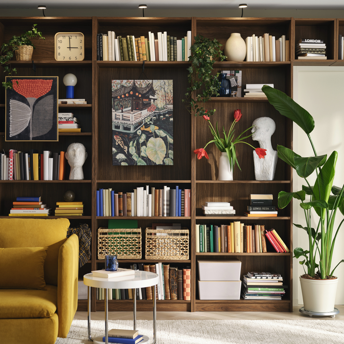 Dark wood bookcase filled with books, artwork, indoor plants, and decorative objects.