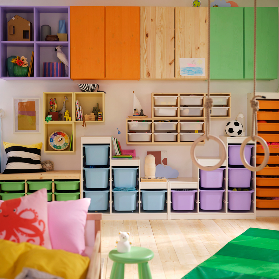 Colorful playroom with modular storage units, plastic bins, and hanging gymnastic rings.