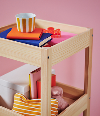 Light wood rolling cart holding a striped cup, colorful books, and desk accessories.