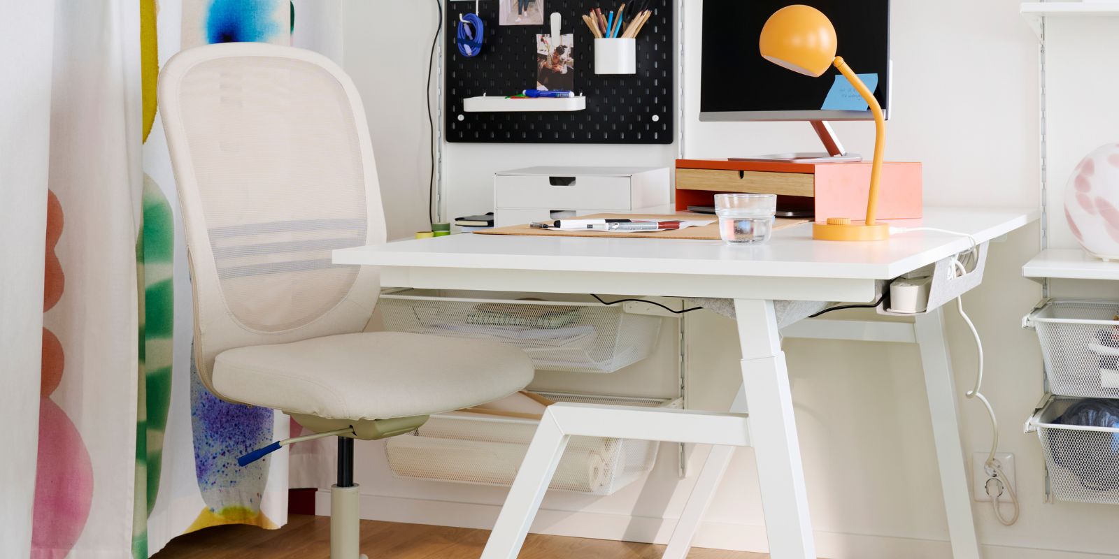 A home office feautures a white TROTTEN desk sit/stand made from electric material, with a chair beside it.