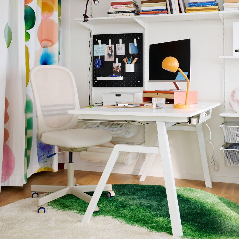 A home office feautures a white TROTTEN desk sit/stand made from electric material, with a chair beside it.