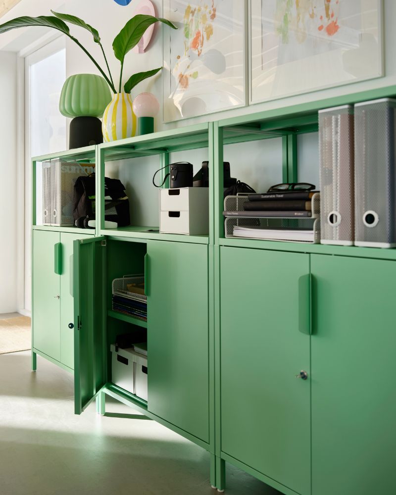 Green modular storage cabinets with lower doors, open shelving, binder organizers, and decorative objects on top.
