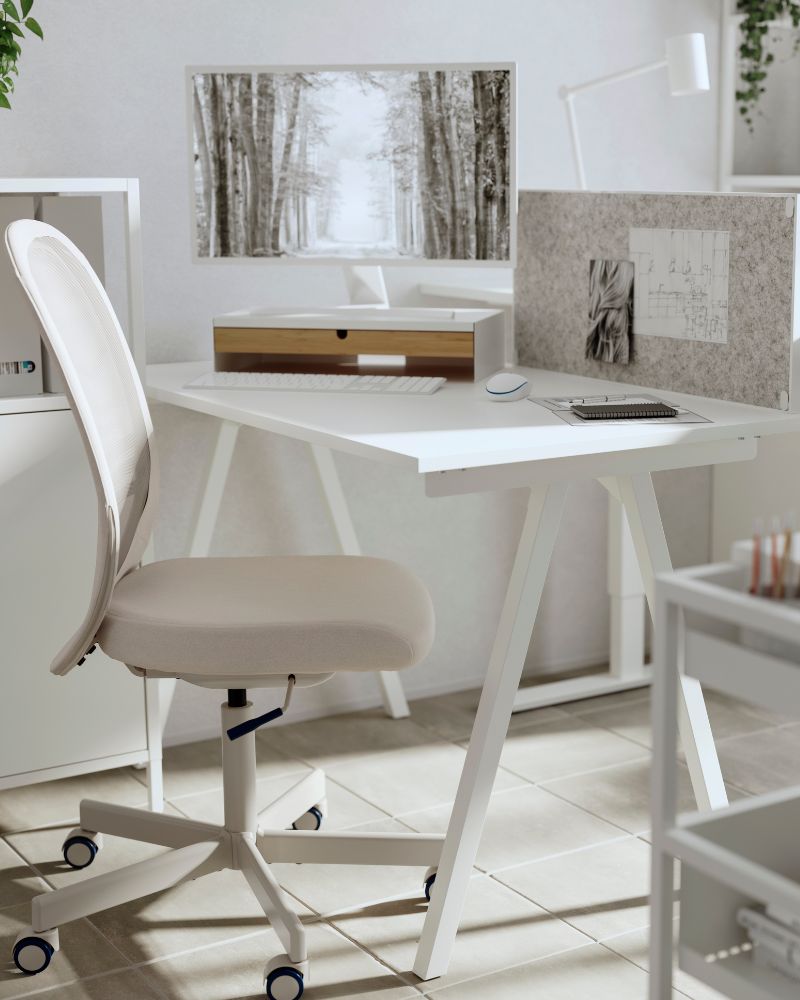 Modern white office setup featuring a light beige ergonomic chair, desk, monitor, felt privacy screen, and organizers in a bright room.