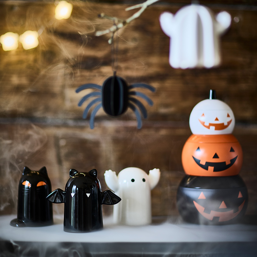 Un estante decorado para Halloween con tres figuras KUSTFYR, un conjunto de latas con forma de calabaza y decoraciones colgantes.