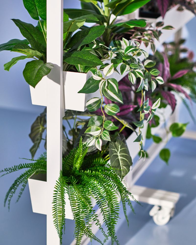 Rincón de trabajo natural con plantas FEJKA y armazones MITTZON con ruedas y recipientes, creando almacenamiento flexible.