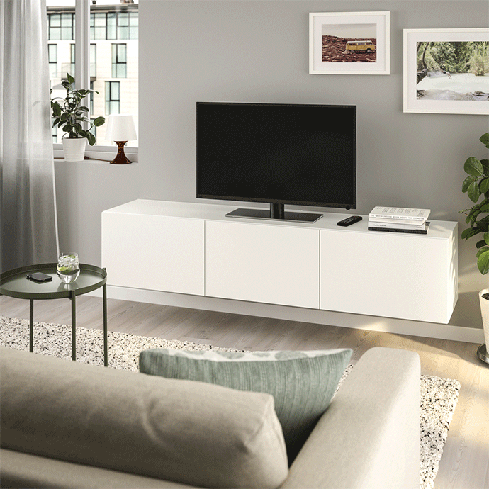 Wall-mounted white TV unit with a black television, dark green side table, textured rug, and modern living room decor.