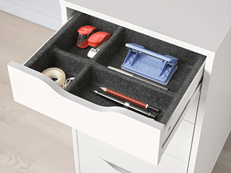 Open top drawer of a white desk unit, organized with dark felt tray compartments holding pens, tape, and a hole punch.