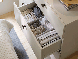 Open white dresser drawer organized with fabric compartment dividers containing neatly folded clothes and socks.