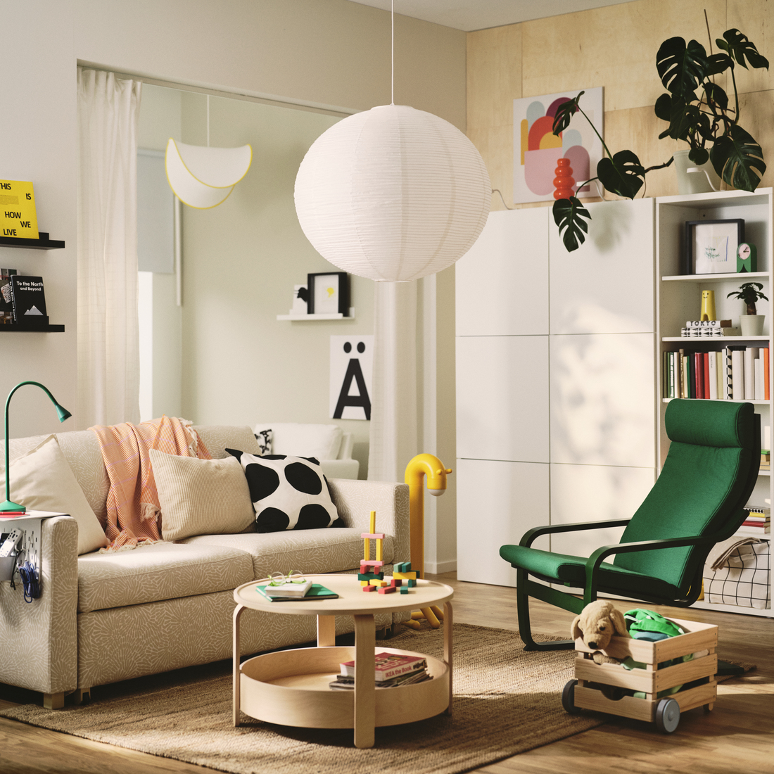 Bright living room with beige sofa, round coffee table, green armchair, white rice paper pendant lamp, and white storage cabinets.