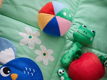 Un sonajero verde de SANDBI, un peluche y un juguete musical, colocados sobre una alfombra de juegos de SANDBI.