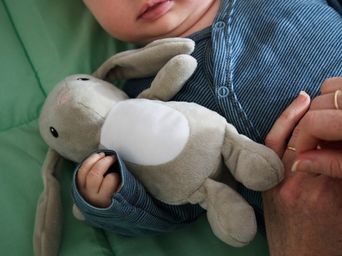 Primer plano de un bebé tumbado en el suelo, vestido con un pijama azul, que sostiene un conejo de peluche de DVARGHARE.