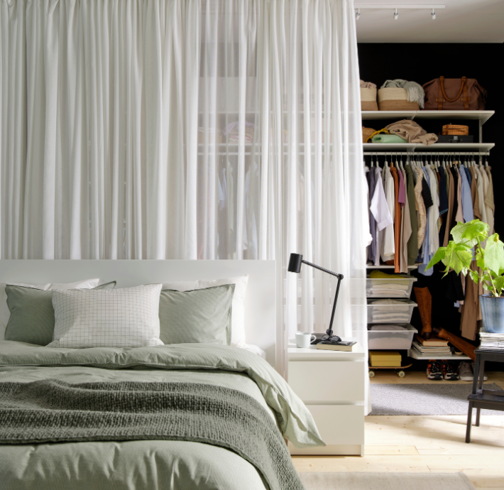 Bedroom with green bedding and a sheer white curtain separating an open closet.