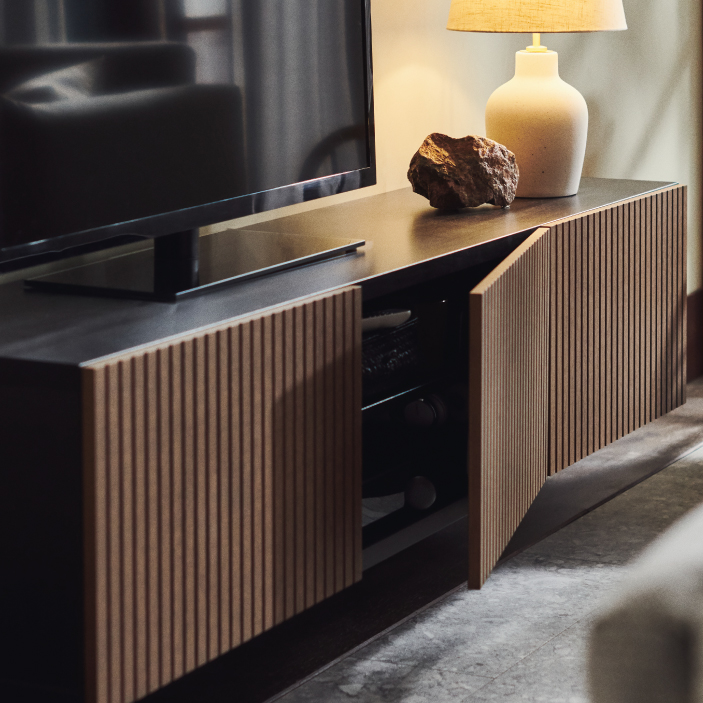 Black TV stand with slatted wood cabinet doors slightly open and a table lamp.