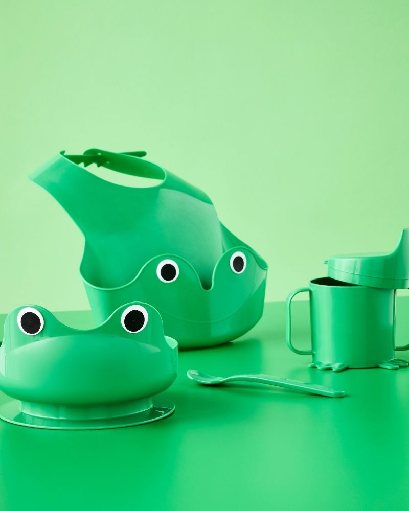 Juego de vajilla para bebé MATA de cuatro piezas en color verde brillante con temática de rana, incluye babero, tazón, vaso con boquilla y cuchara.