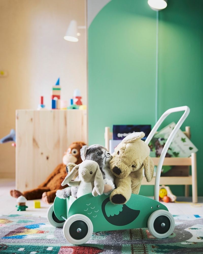 Andador para niños pequeños UPPSTÅ completamente lleno de peluches, con una pared verde detrás y la alfombra VALLABY debajo.