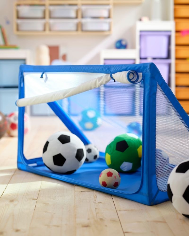 Una portería y almacenaje de pelotas azul SPORTSLIG, llena de balones de fútbol de peluche SPARKA.