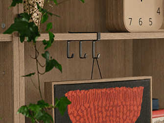 Dark wood sideboard unit with closed doors and open shelves storing books, woven baskets, plants, and a white vase.