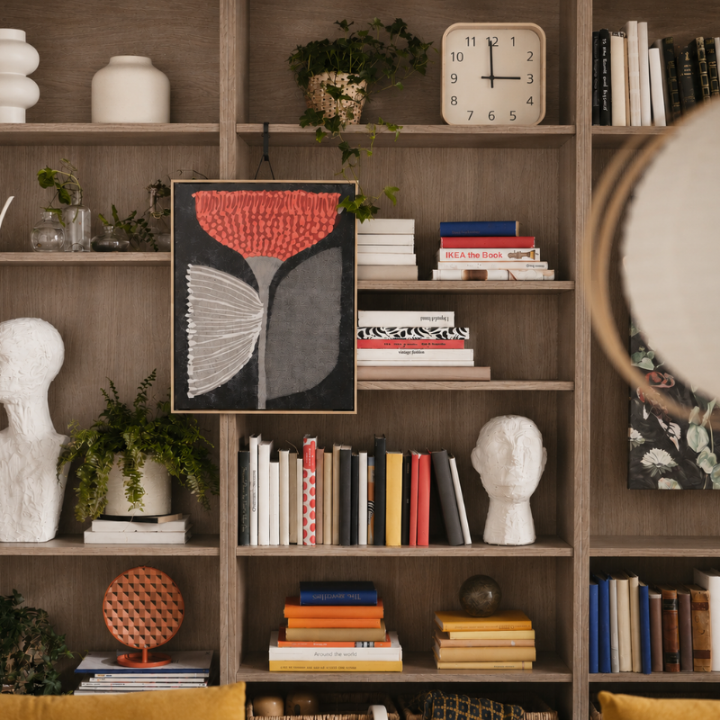 El salón cuenta con una estantería BILLY marrón con libros, objetos decorativos y plantas, lo que crea un espacio cálido y acogedor.