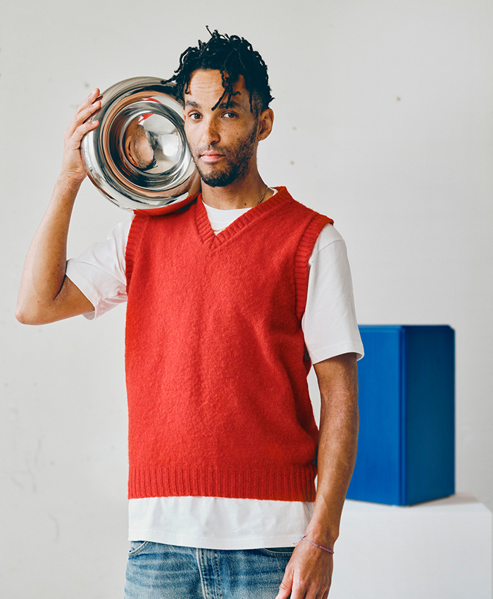 Person holding a reflective metallic vase in a minimalist setting with red and blue accents.