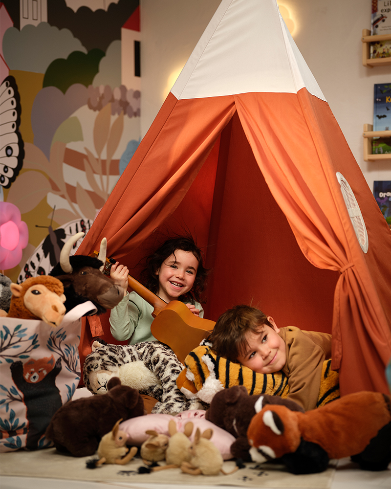 Dos niños en una tienda HÖVLIG juegan con peluches ALPTALL, incluyendo a los tigres Bengalís y el panda rojo.
