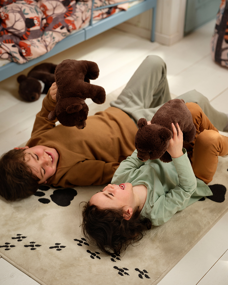 Niños tumbados sobre la alfombra ALPTALL y jugando con peluches de osos asiáticos ALPTALL.
