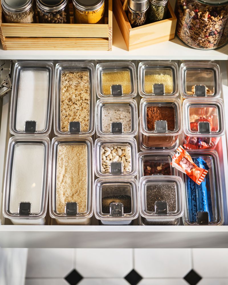 Un cajón de cocina organizado con tarros para alimentos secos KORALLVIPPA con tapa, en los que se guardan azúcar, frutos secos, avena, especias y otros alimentos.