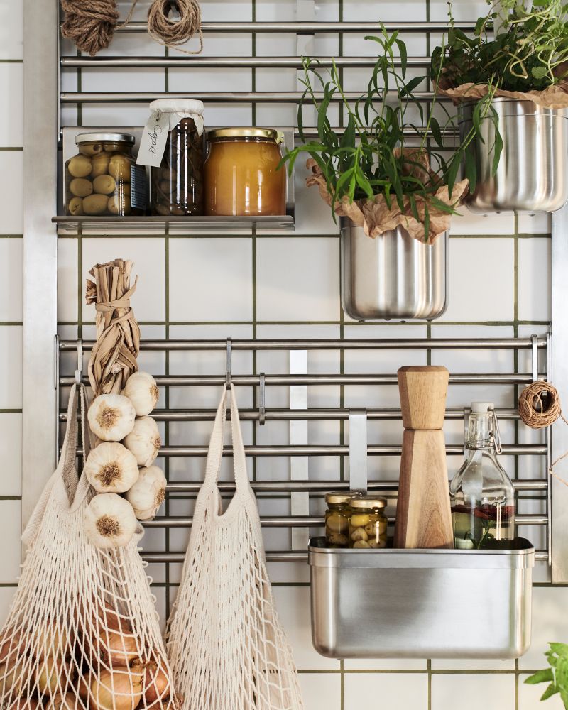 Una rejilla de pared KUNGSFORS de acero inoxidable equipada con varios estantes para recipientes y bolsas de malla.