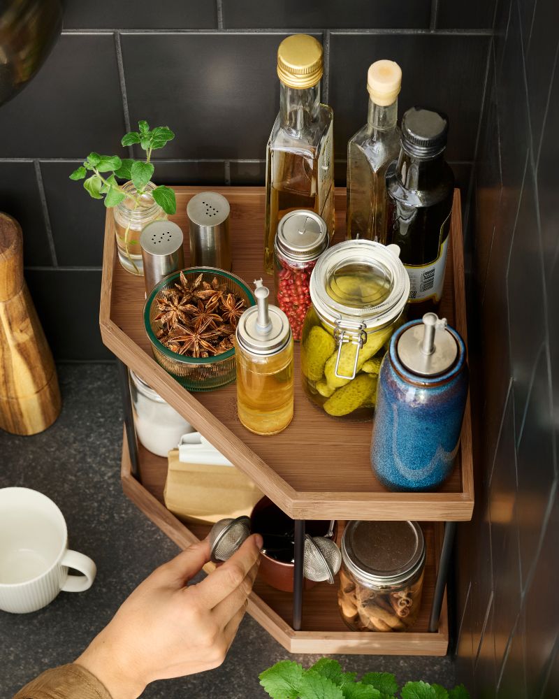 Una estantería de esquina NÅLBLECKA de metal y bambú llena de especias y condimentos sobre la encimera de una cocina.