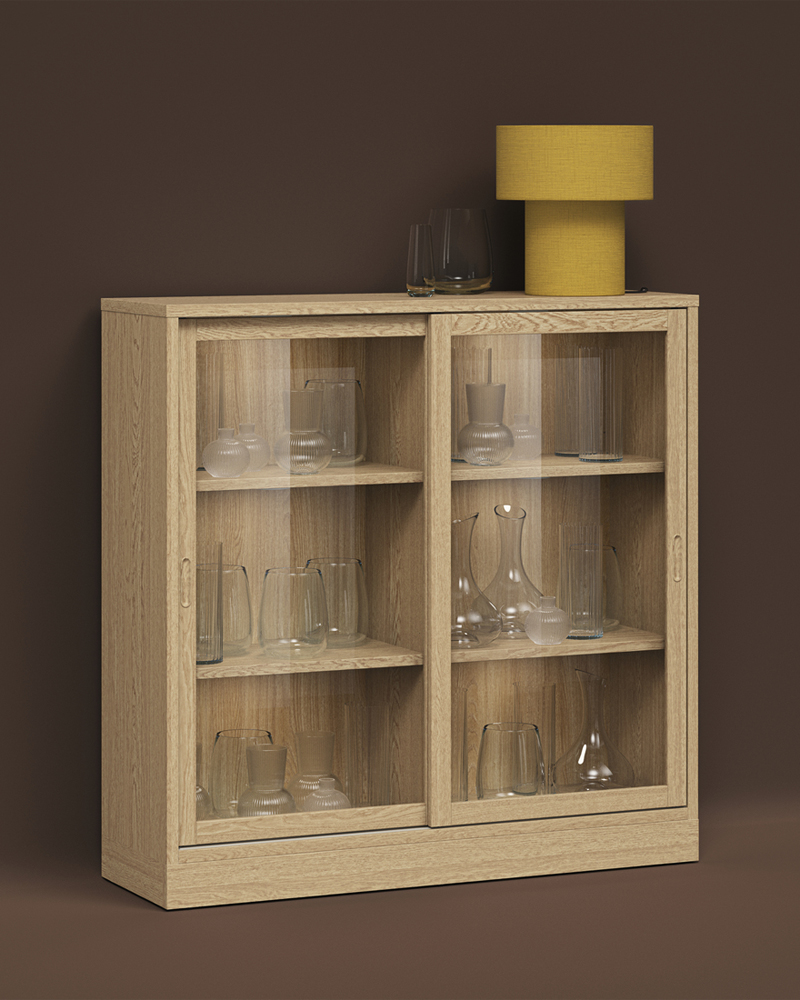 A STOCKHOLM table lamp atop a TONSTAD oak-veneer cabinet holding glassware, all set against a brown background.