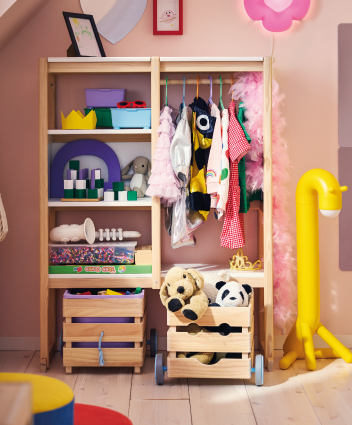 Wooden children's wardrobe with hanging clothes, shelving toys, and wooden crates with plushies.