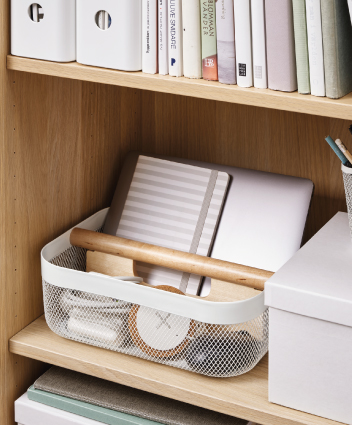 Wire mesh basket with wooden handle organizing a notebook and laptop on a shelf.