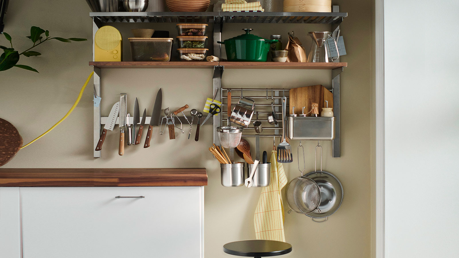 Una pared de la cocina equipada con estantes abiertos, barras y un soporte magnético para cuchillos, todos ellos repletos de utensilios de cocina de uso diario.