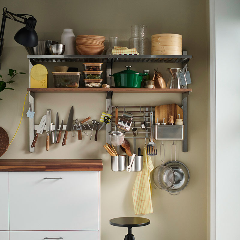Una pared de la cocina equipada con estantes abiertos, barras y un soporte magnético para cuchillos, todos ellos repletos de utensilios de cocina de uso diario.