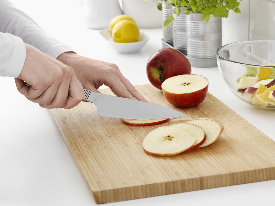 A person slices an apple with a knife on a wooden board.
