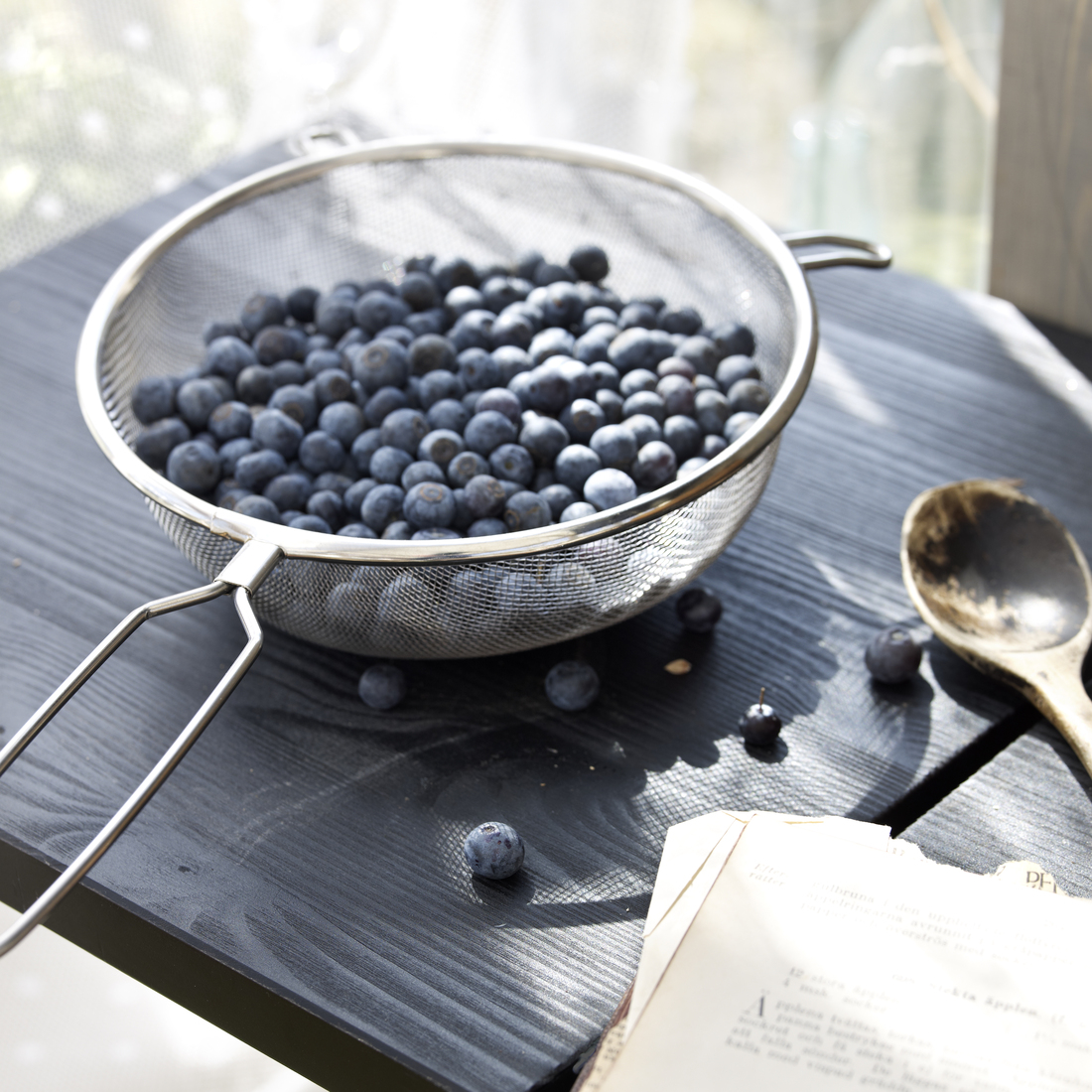 A metal sieve filled with fresh blueberries sits on a dark wooden table.