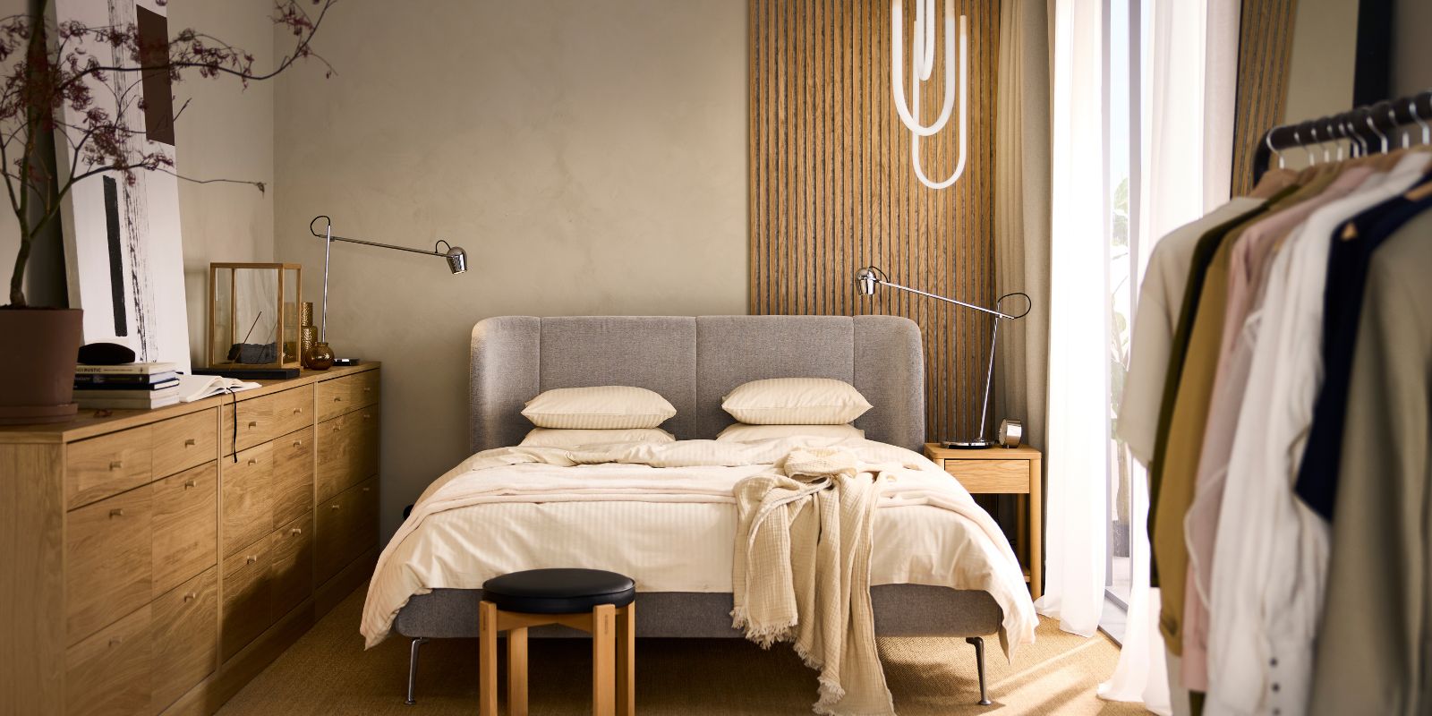 Dormitorio moderno con cama gris, cómoda de madera, perchero y detalles cálidos. Ambiente acogedor.