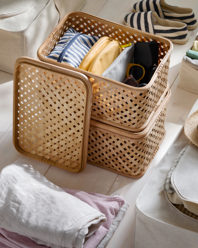 Caja organizadora de mimbre con ropa doblada sobre una cama en un dormitorio ordenado.