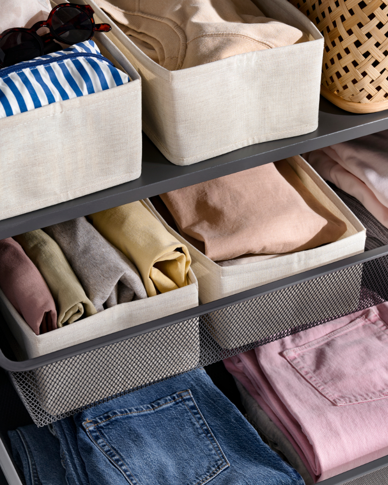 Cajas organizadoras de tela con ropa doblada, ordenadas en estantes de un armario.